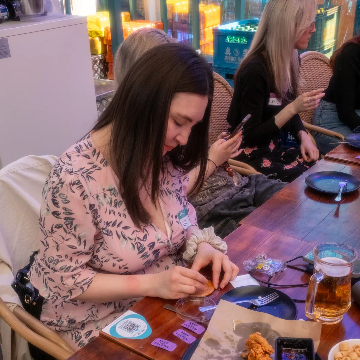 Teacher carefully picking out a Squid Game dalgona shape at the Korvia Spring Party 2026 — purple raffle tickets visible on the table
