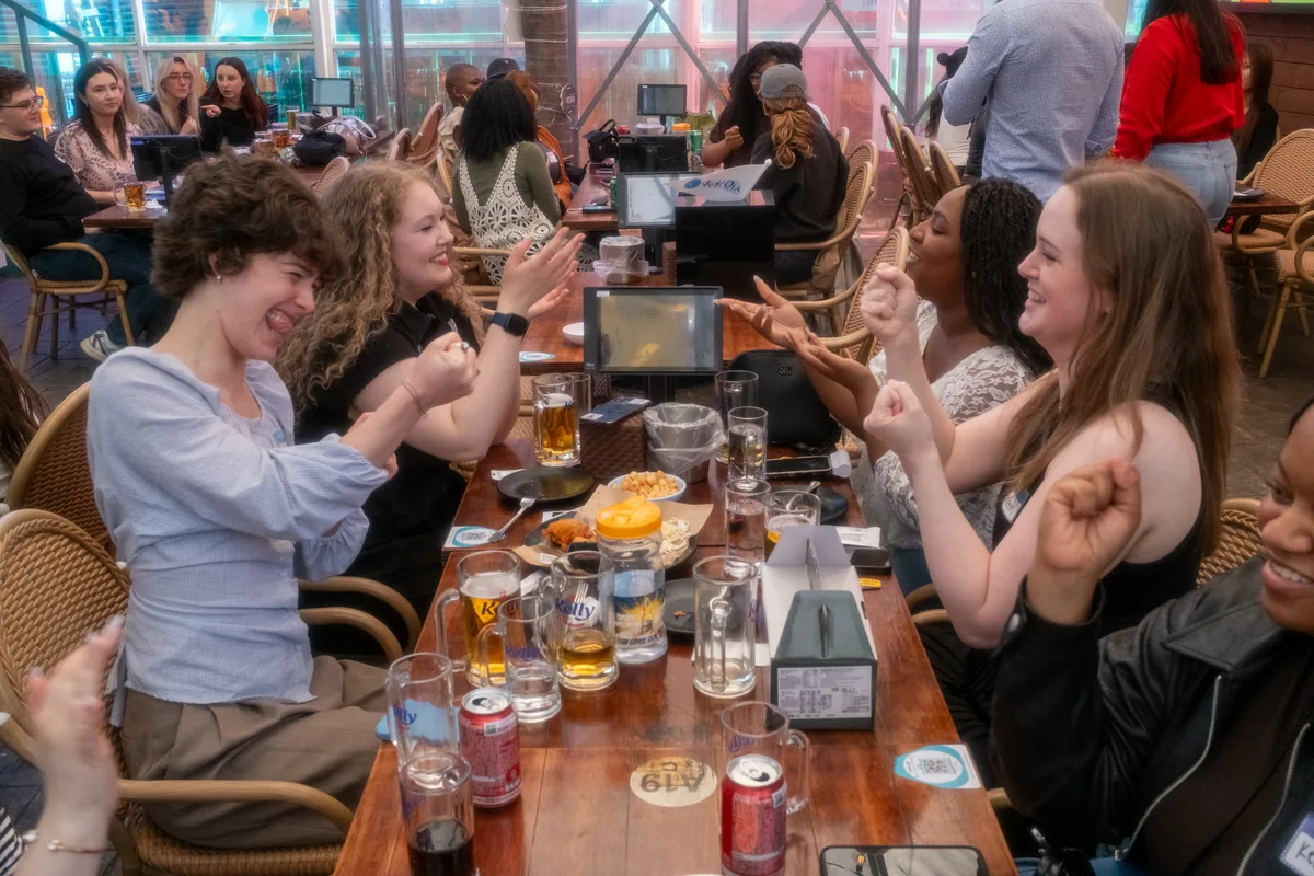 ESL teachers cheering and high-fiving across a long table during the Blooket quiz at Korvia Spring Party 2026